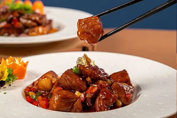closeup of a wagyu beef cube being picked up by chopsticks from a plate of stir-fried wagyu beef with a foreground of another plate of wagyu beef